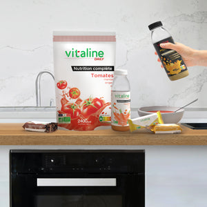 Vitaline Tomates en sachet avec un bol trois bouteilles de Vitaline Carottesavec barre Bananes Carottes Cacao et bouteille Vitaline Catalyst Focus posés sur un plan de travail en bois dans une cuisine